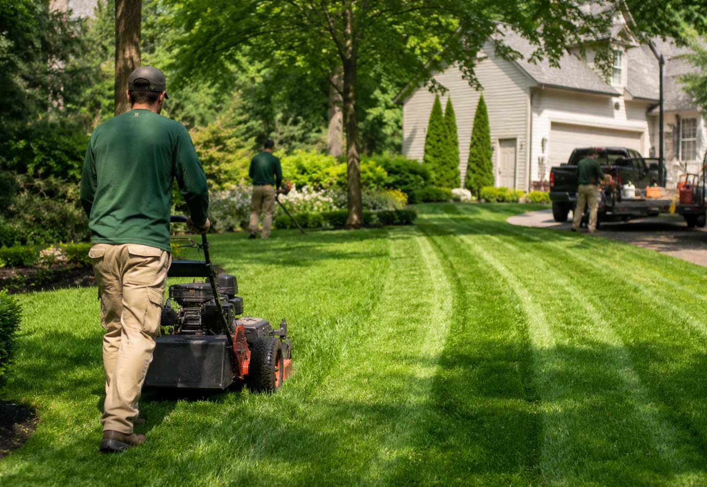Two-person lawn care crew mowing fresh stripes into a residential lawn in Apex, NC